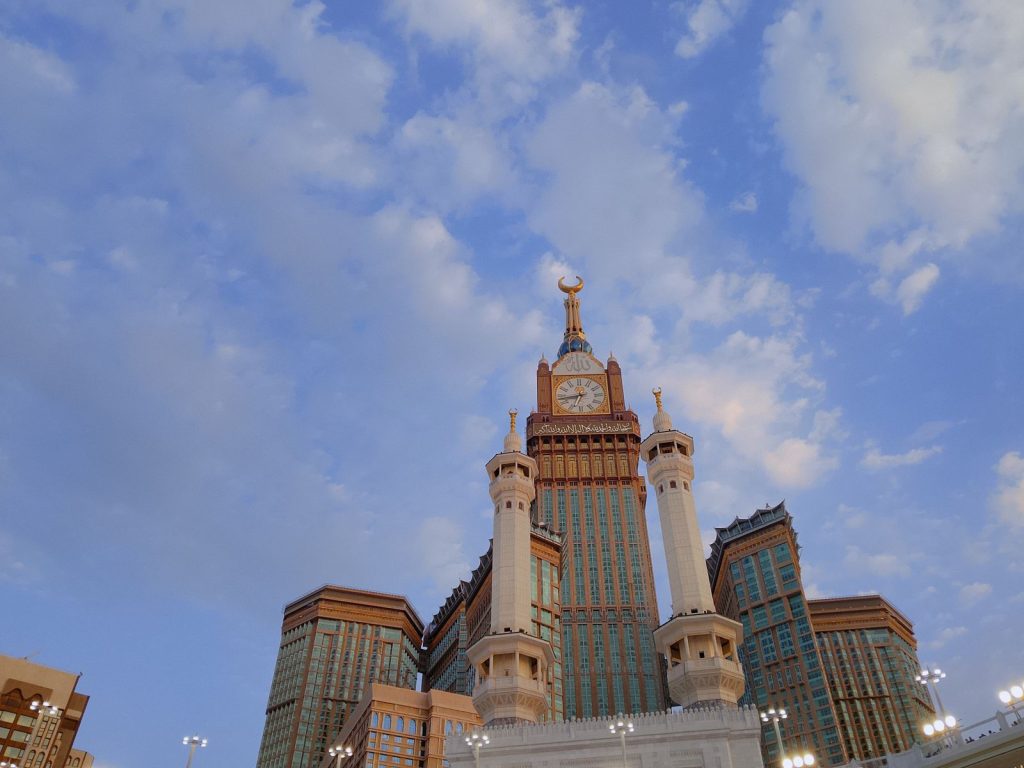 Majestic view of Abraj Al Bait Towers in Mecca with a clear blue sky and scattered clouds.