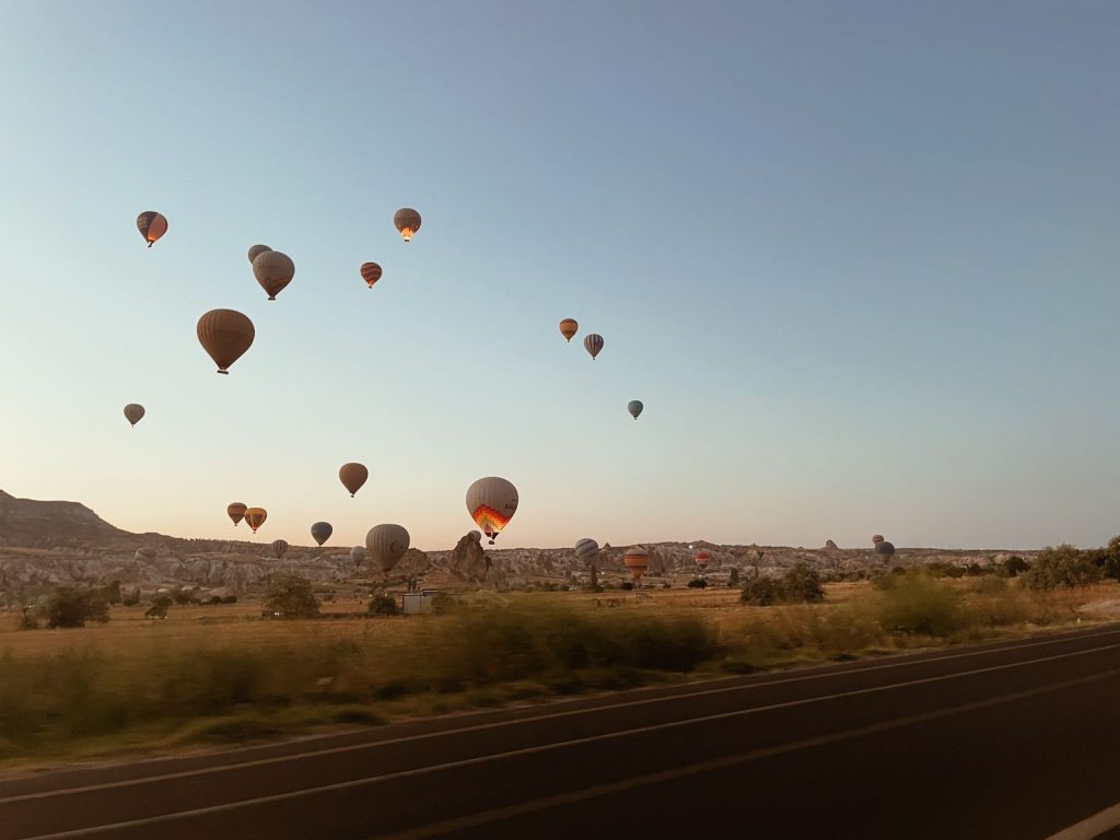 Scenic view of hot air balloons floating over the Cappadocia landscape at sunrise in Türkiye.